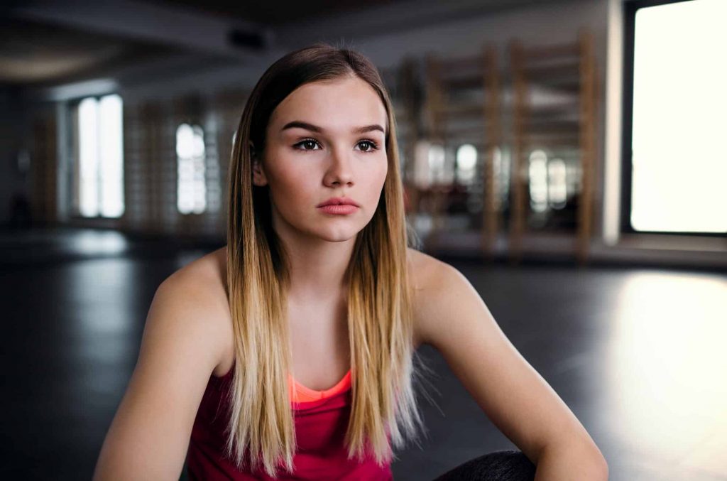 A portrait of young sad girl or woman sitting in a gym.